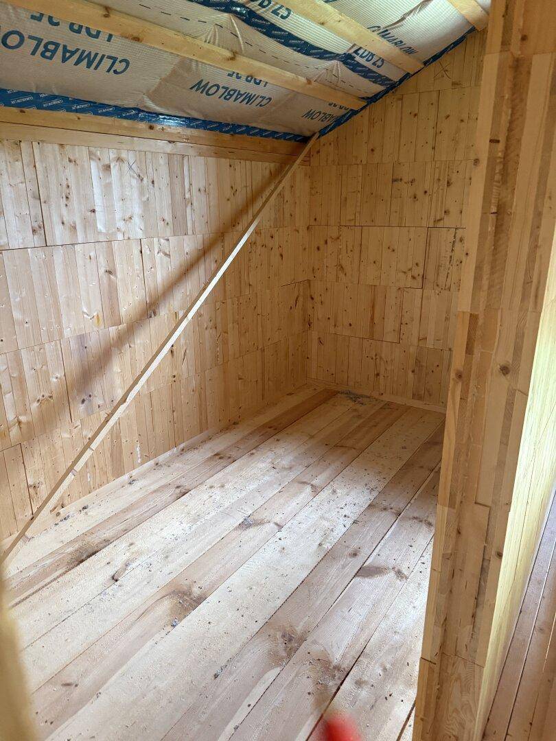 Leeres Dachgeschoss mit Holzwänden, Dachschräge und Holzdielenboden, bereit zum Ausbau.