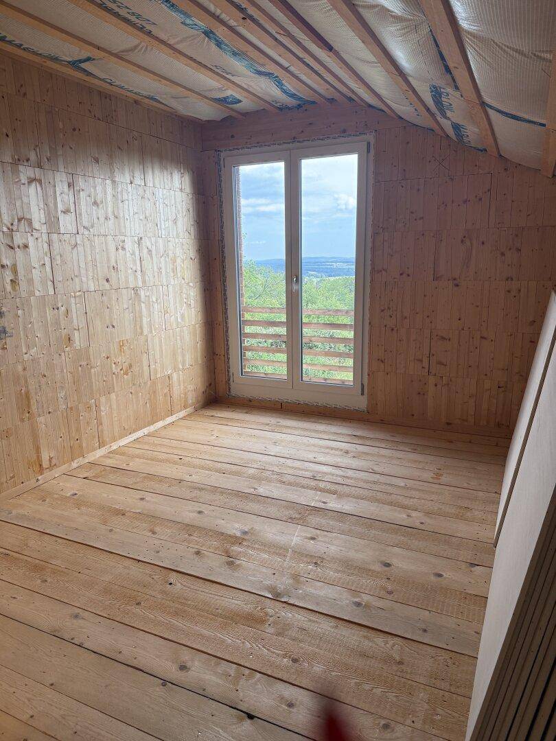 Helles Dachzimmer mit Holzdielenboden, Dachschräge und weitem Ausblick über die Landschaft.
