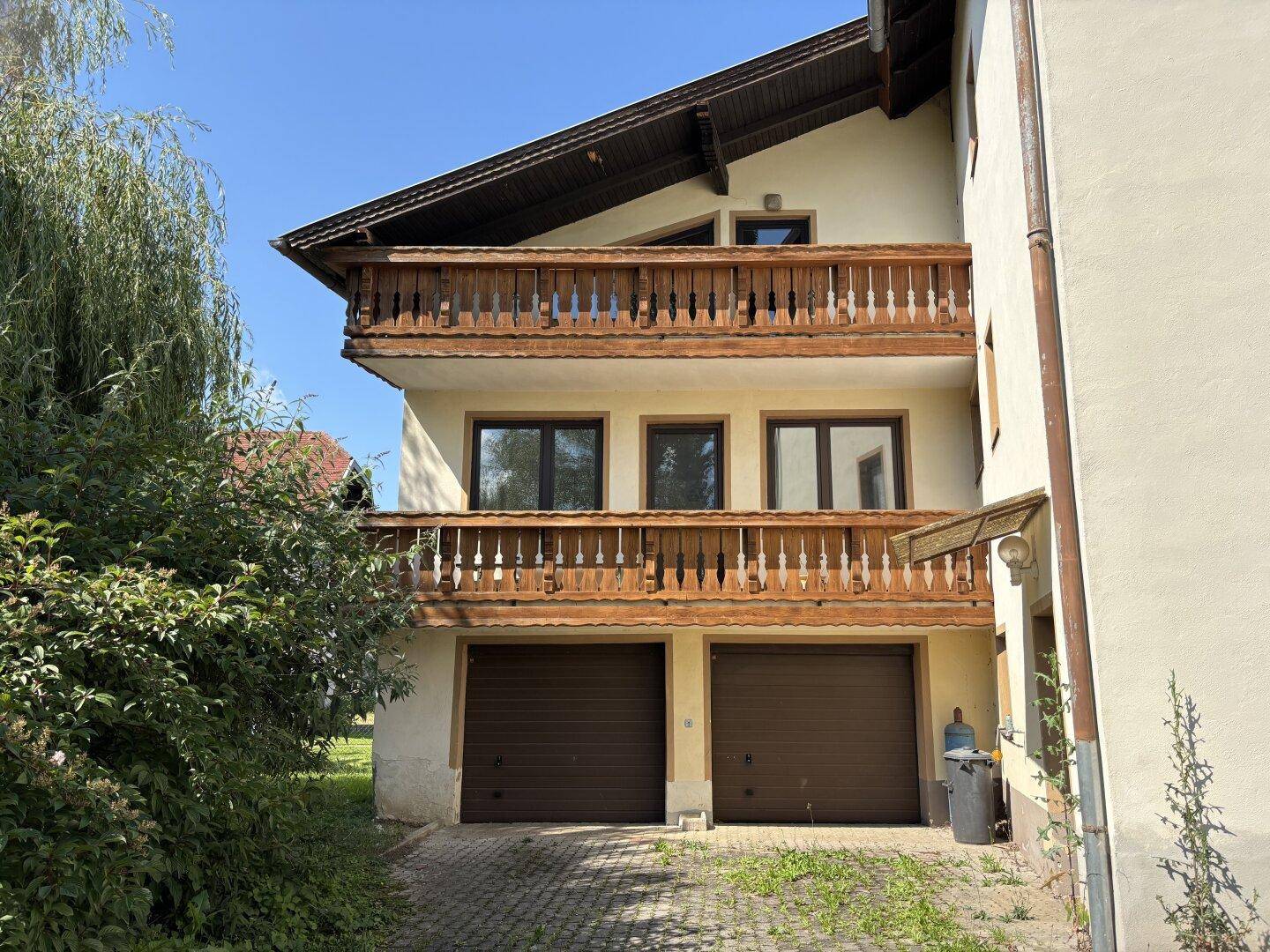Rückansicht des Hauses mit zwei Garagen und darüberliegenden Balkonen mit Holzgeländern.