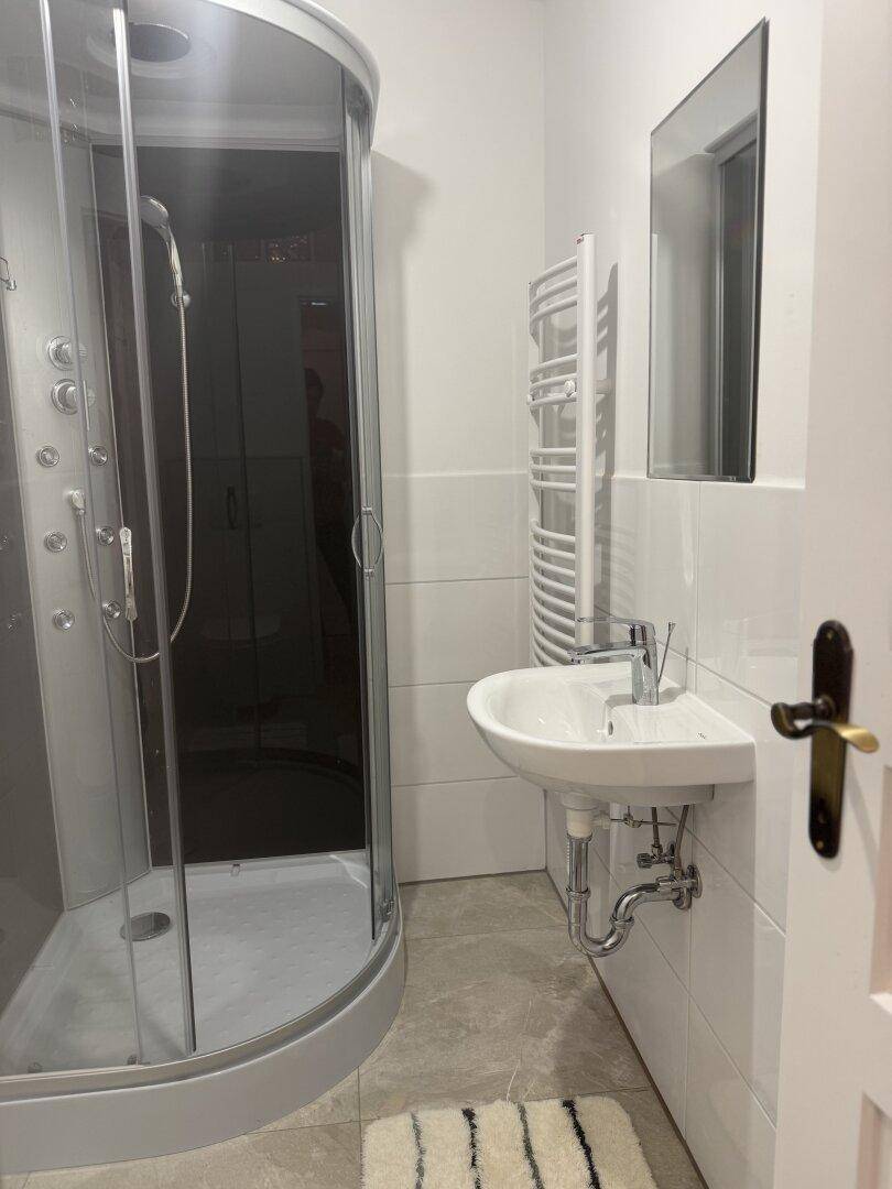 Modernes Badezimmer mit Duschkabine, Wandwaschbecken und beheiztem Handtuchhalter.