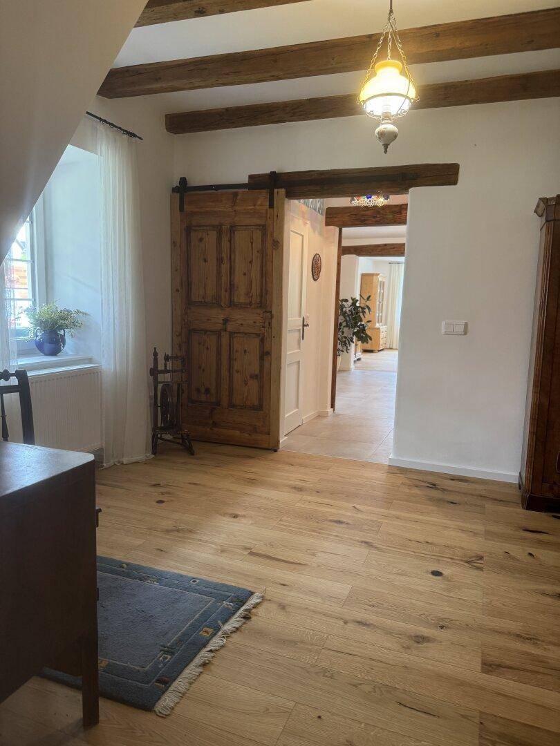 Heller Flur mit Holzboden, sichtbaren Holzbalken und einer rustikalen Schiebetür.