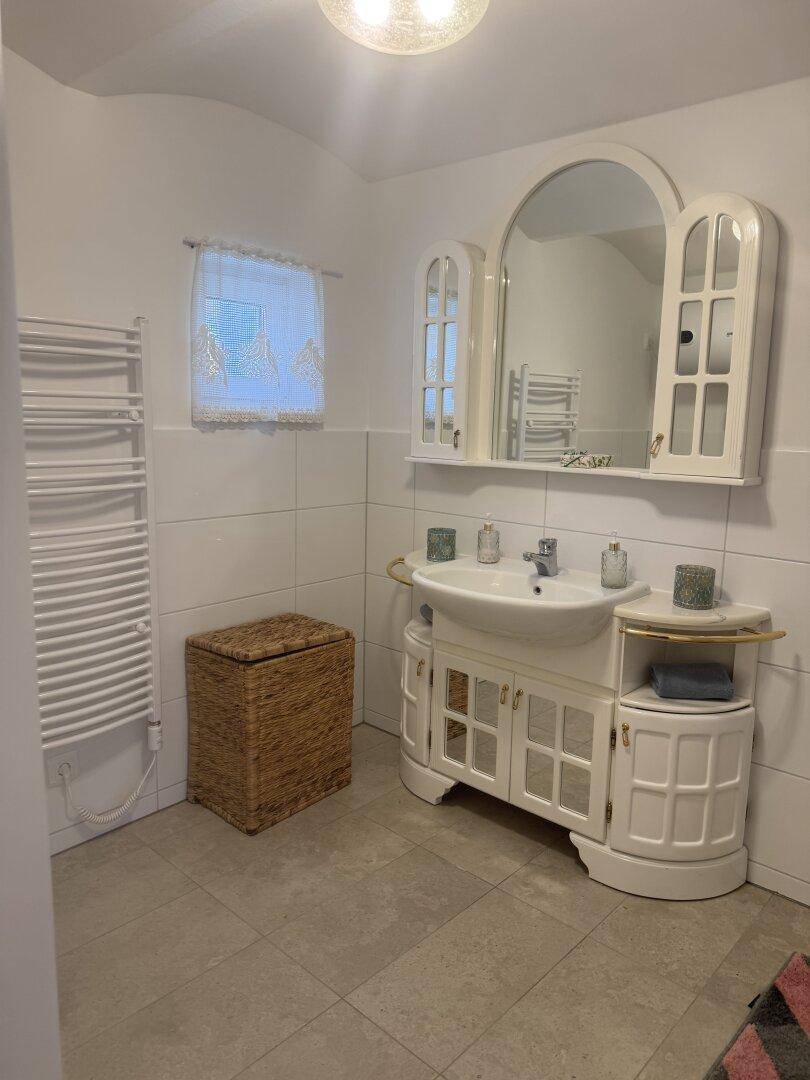 Helles Badezimmer mit Fenster, Waschtischunterschrank und beheiztem Handtuchhalter.