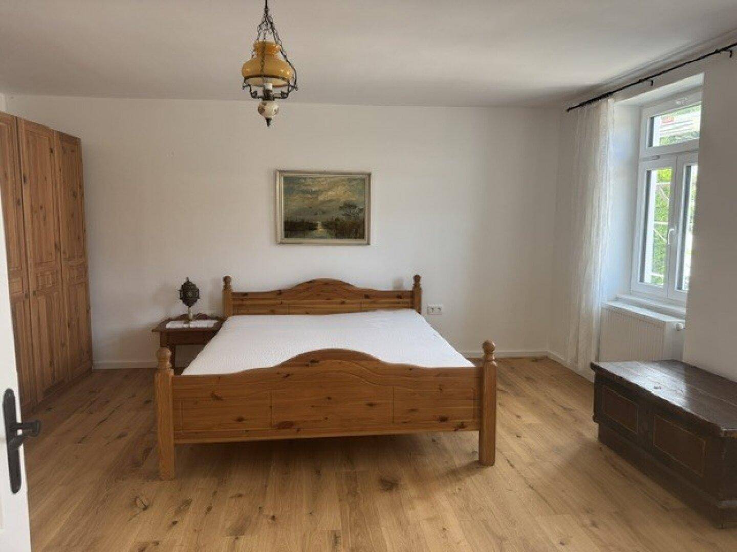 Helles Schlafzimmer mit Holzbett, passendem Schrank und Holzboden, durchflutet von Tageslicht.