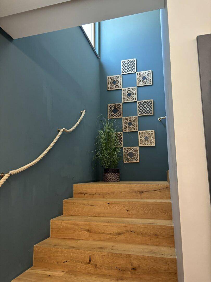 Moderner Treppenaufgang mit Holzstufen, blauer Wand und dekorativen Wandelementen.