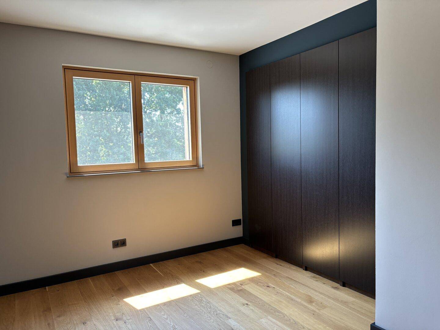 Schlafzimmer mit Holzboden, Fenster und einem integrierten, dunklen Kleiderschrank.