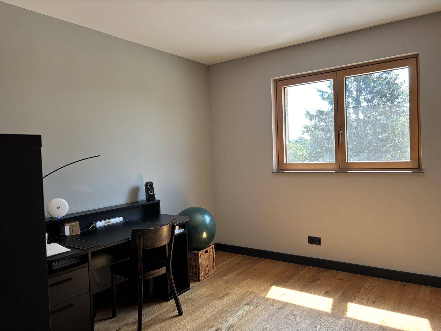 Arbeitszimmer mit Schreibtisch, Bürostuhl und einem Fenster, das viel Tageslicht hereinlässt.
