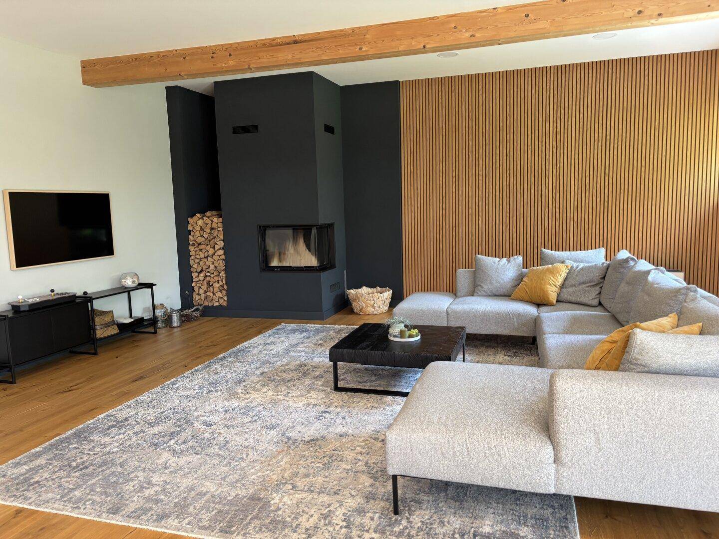 Geräumiges Wohnzimmer mit Holzboden, Kamin, großem Sofa und einem modernen TV-Bereich.