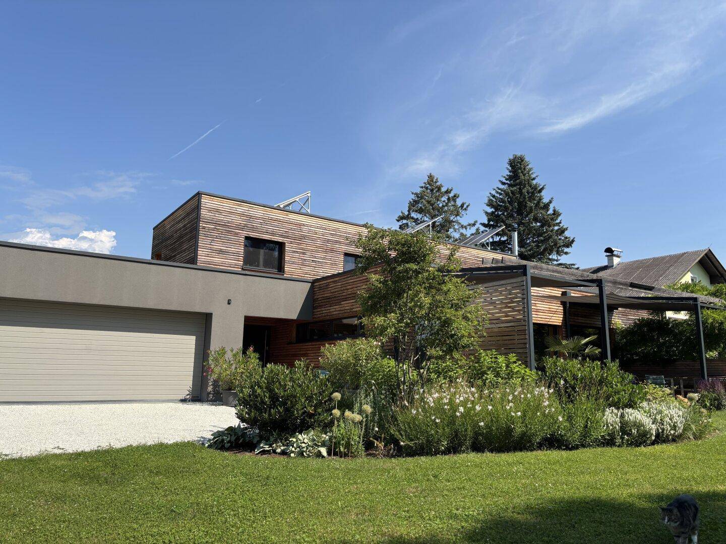 Moderne Hausfassade mit Holzverkleidung, integrierter Garage und gepflegtem Vorgarten unter blauem Himmel.