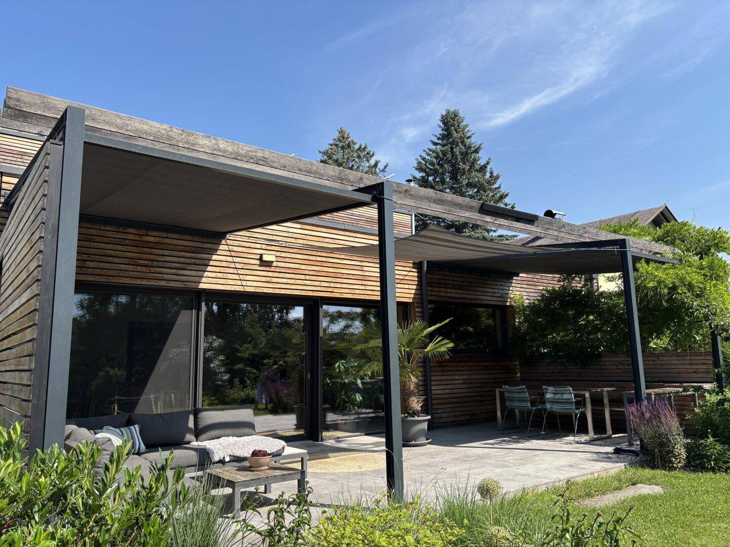 Großzügige Terrasse mit moderner Pergola, bequemen Loungemöbeln und Zugang zum Gartenbereich.