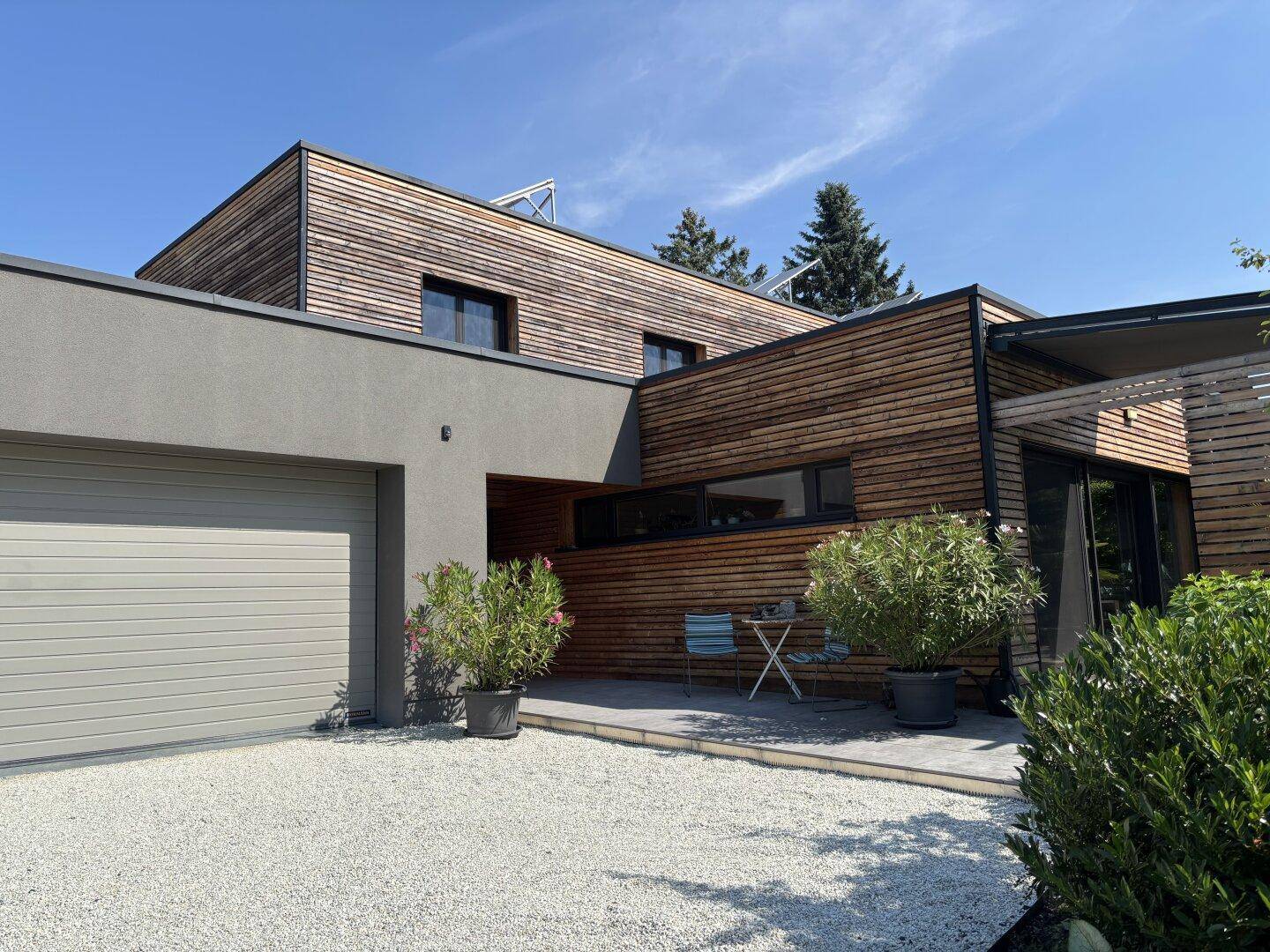 Ansicht des modernen Hauses mit Holzfassade, Garage und gepflegter Kiesauffahrt an einem sonnigen Tag.