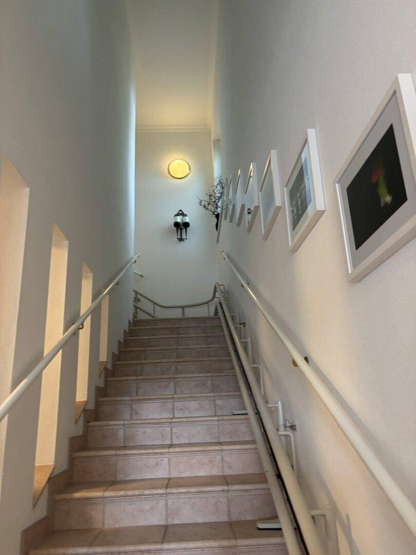 Helles Treppenhaus mit gefliesten Stufen und einem Handlauf entlang der Wand.