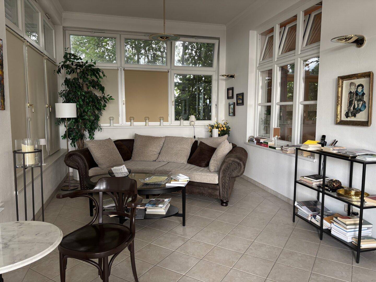 Geräumiger Wohnbereich mit vielen Fenstern, bequemer Couch und dekorativen Regalen.