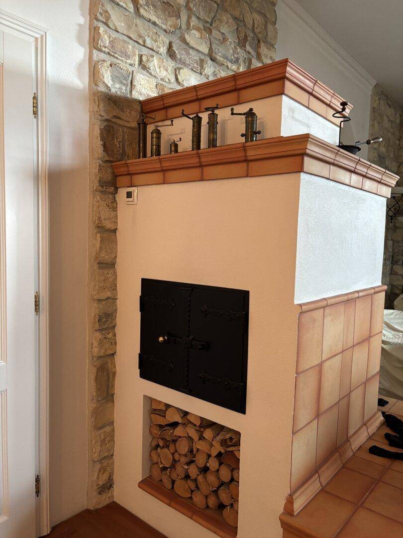 Traditioneller Kachelofen mit Holzscheiten und rustikaler Steinwand, der Wärme und Gemütlichkeit spendet.
