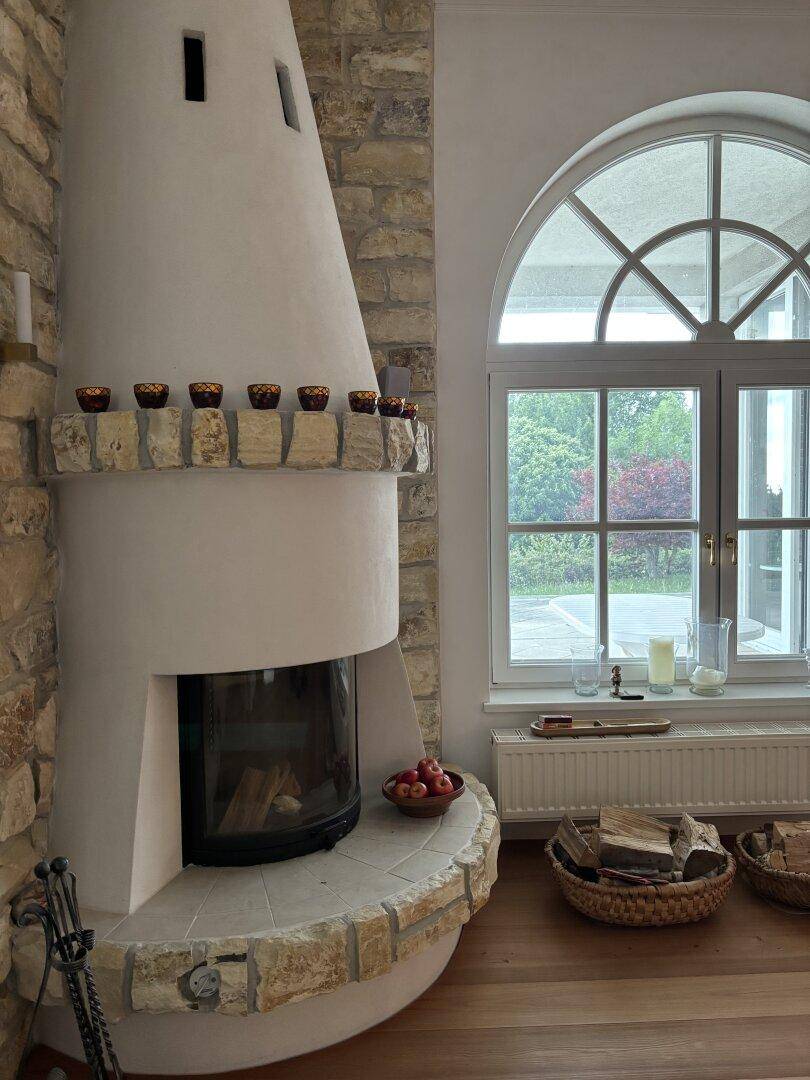 Gemütlicher Wohnbereich mit Kamin, großen Bogenfenstern und Blick ins Grüne.