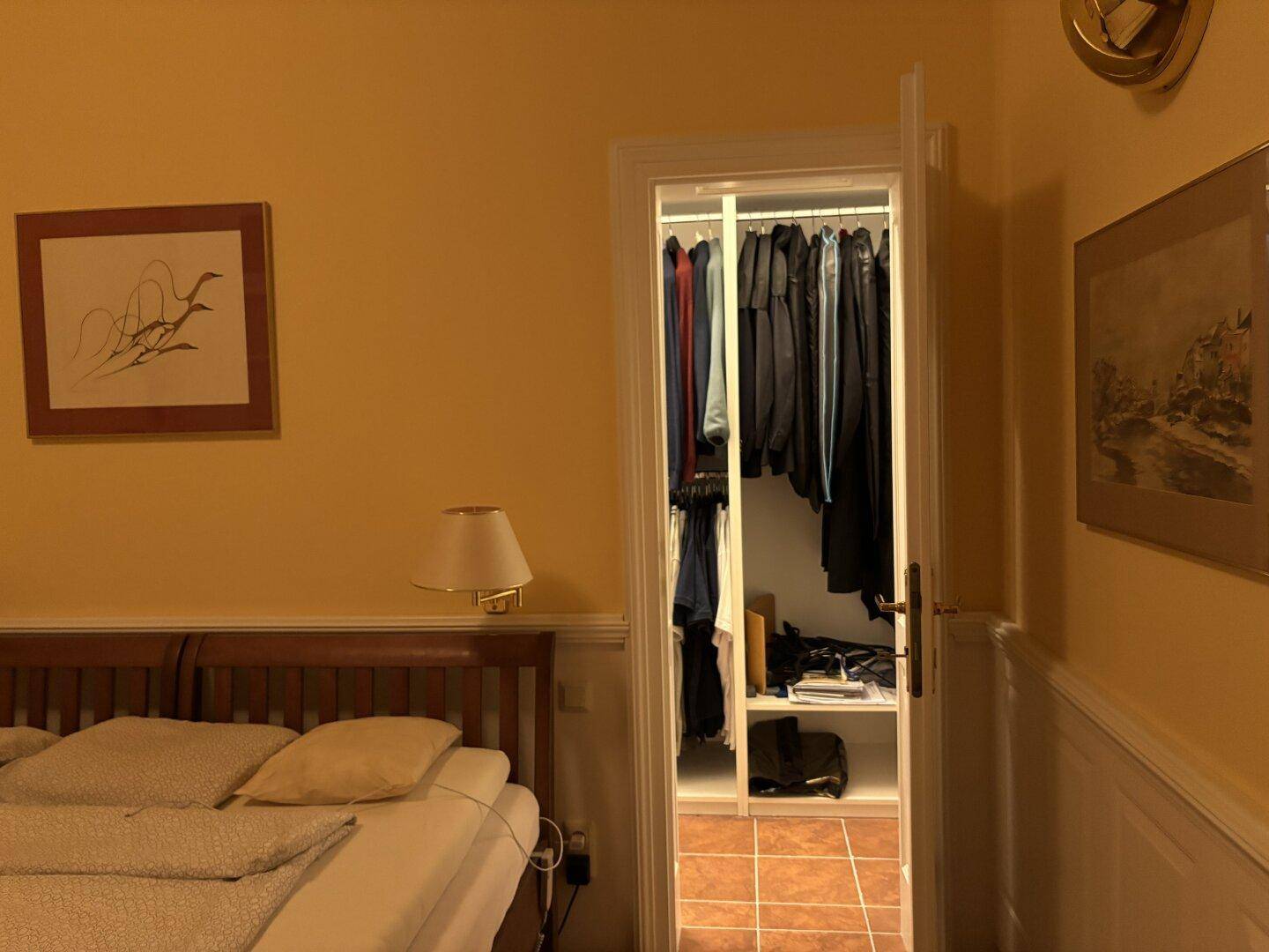 Schlafzimmer mit gelben Wänden und Blick in den angrenzenden begehbaren Kleiderschrank.