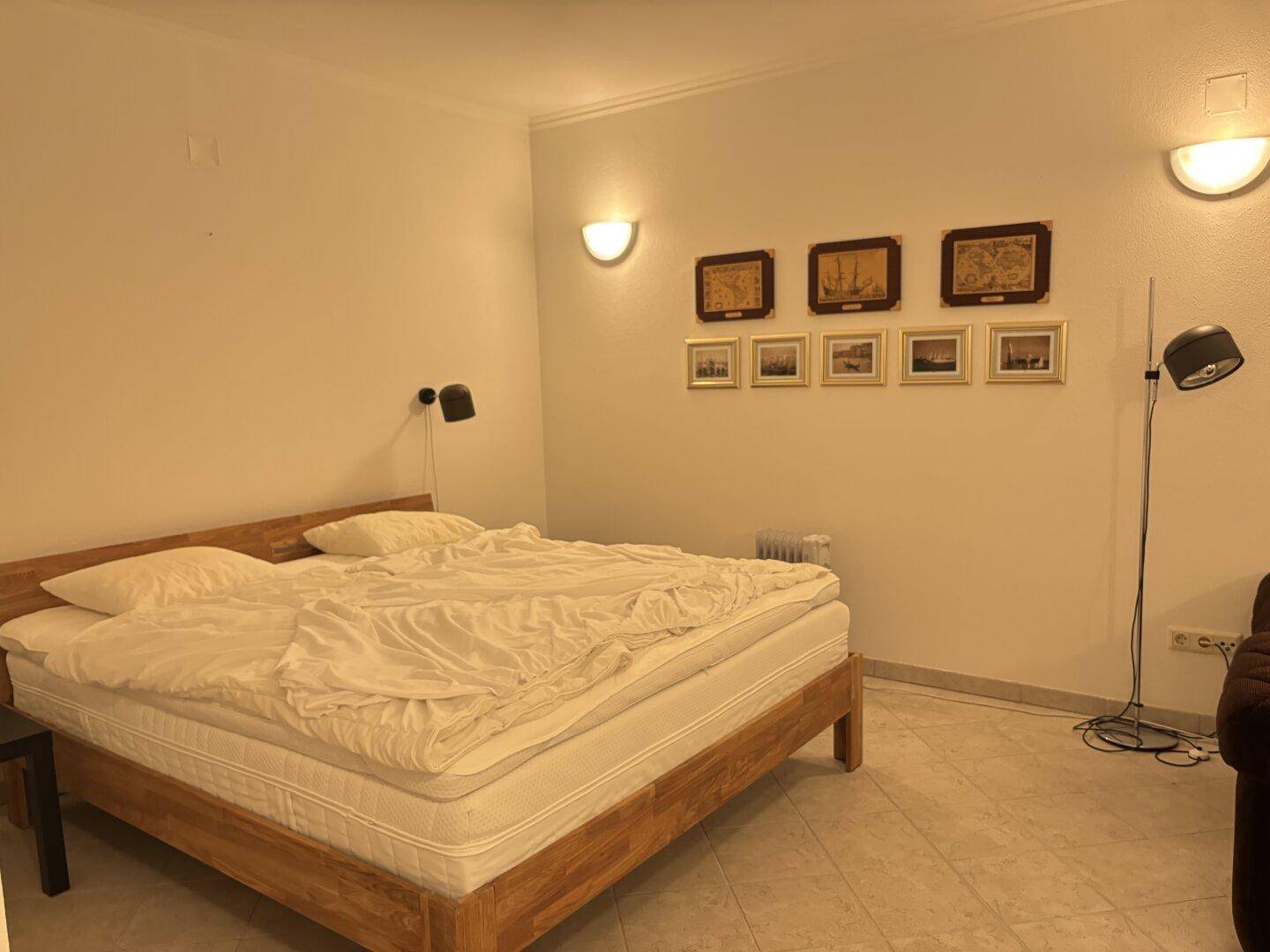 Schlafzimmer mit Doppelbett und schlichter Einrichtung, beleuchtet von Wandlampen.