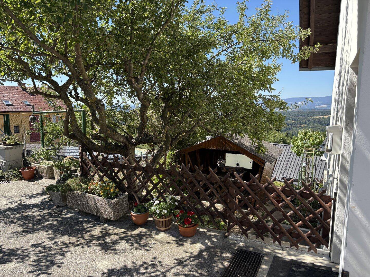 Terrasse mit Blumenkübeln, Holzzaun und Blick auf die Landschaft, einladend und sonnig.