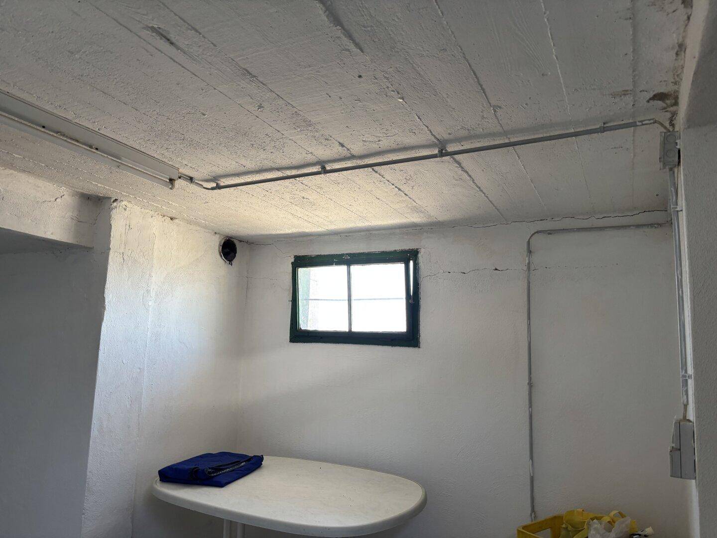 Kellerraum mit kleinem Fenster, Betonwänden und sichtbaren Leitungen, ideal als Abstellraum.