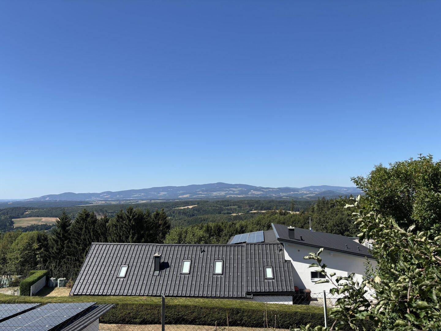 Weitläufiger Blick über bewaldete Hügel und Täler unter klarem blauem Himmel, der eine ruhige Landschaft zeigt.