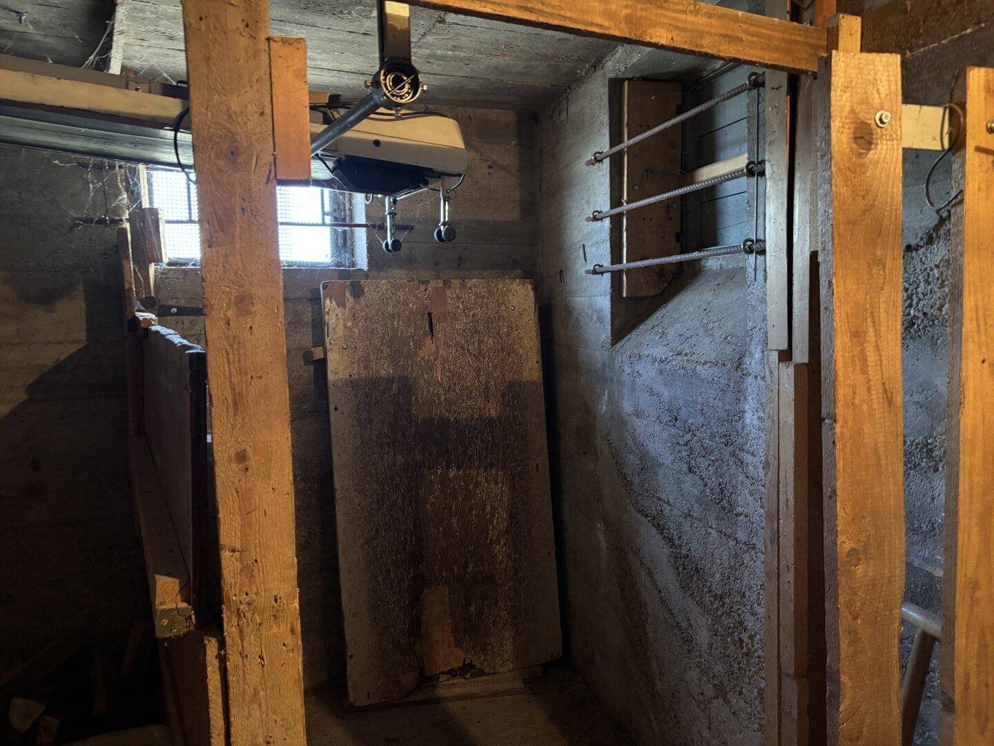 Unfertiger Kellerraum mit Betonwänden, Holzbalken und einem kleinen Fenster.