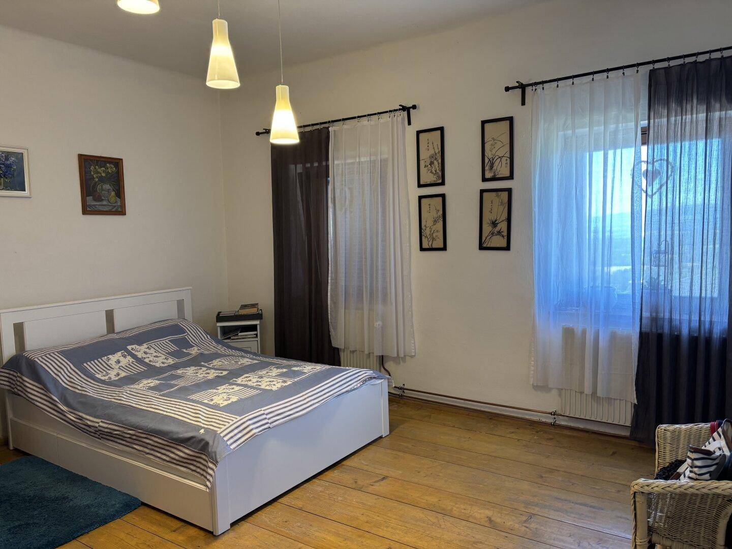 Schlafzimmer mit Holzboden, Doppelbett und großen Fenstern mit Blick ins Grüne, sehr hell.