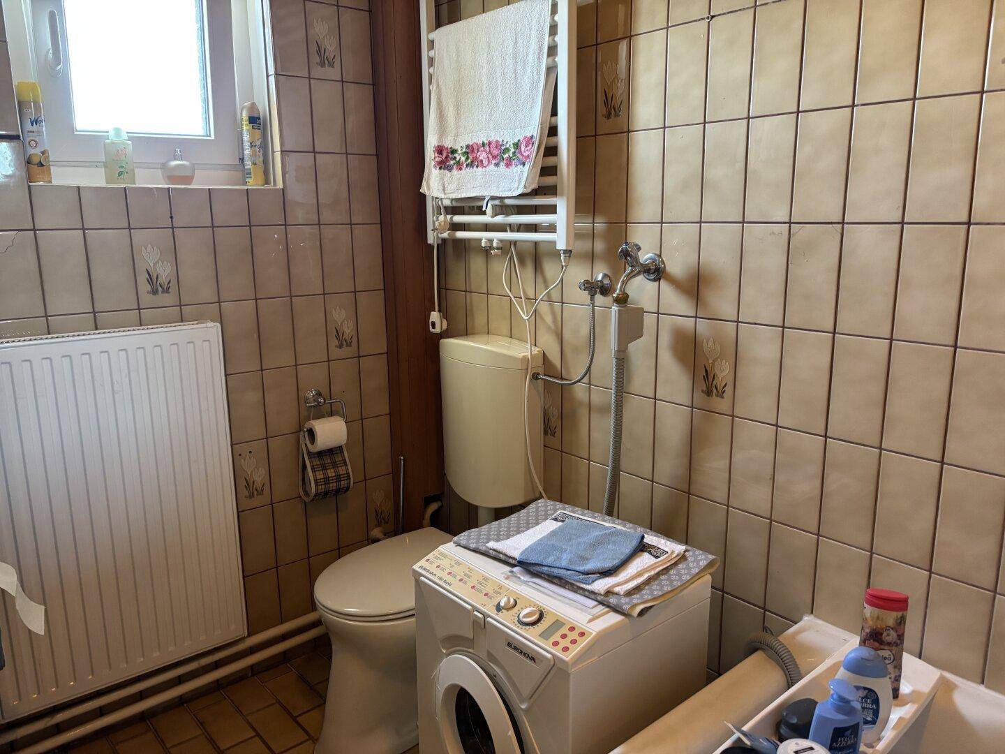 Badezimmer mit Toilette, Waschmaschine und beheiztem Handtuchhalter, praktisch und funktional.