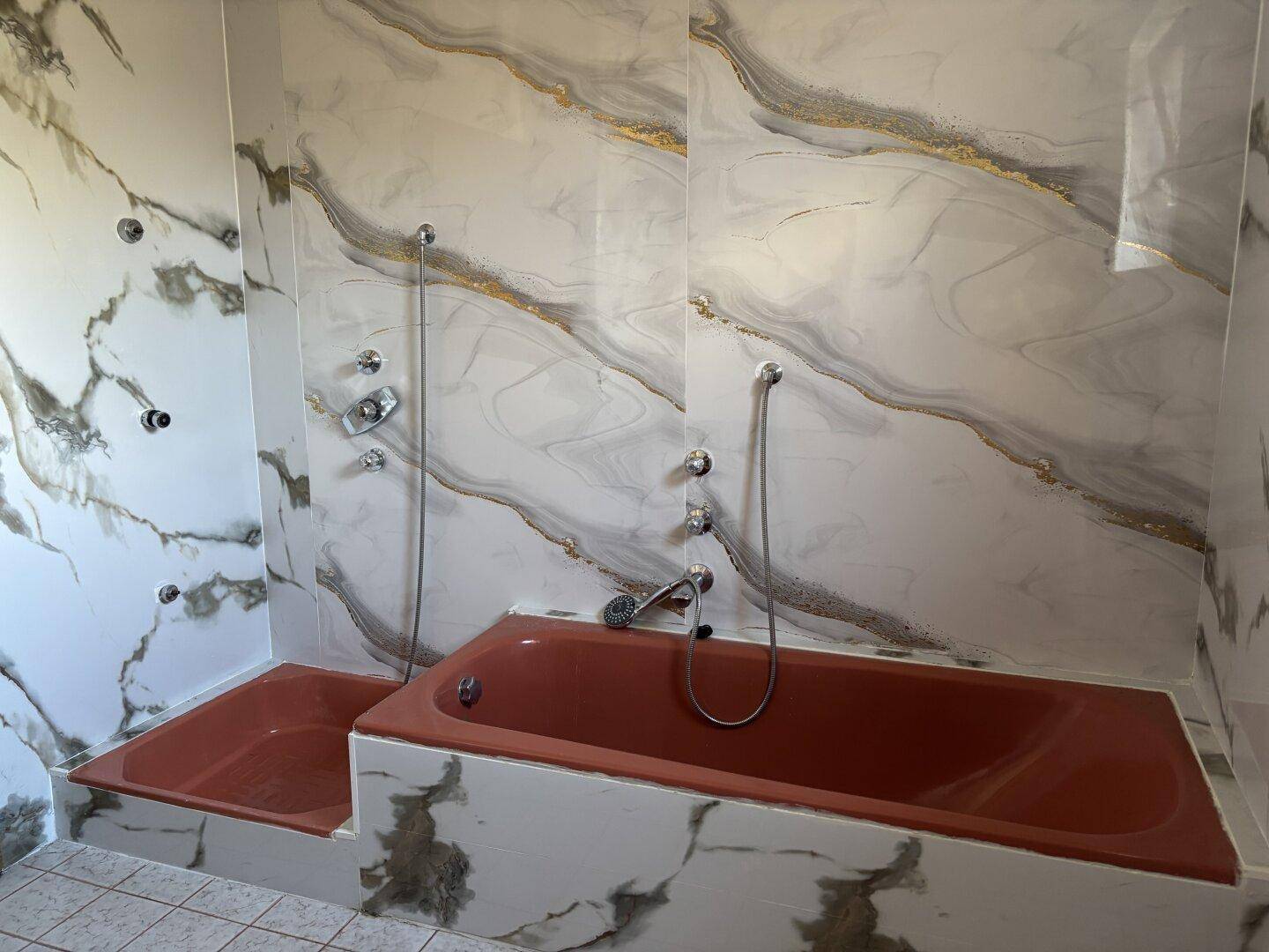 Badezimmer mit einer roten Badewanne, Duschbereich und auffälligen Marmor-Effekt-Fliesen.
