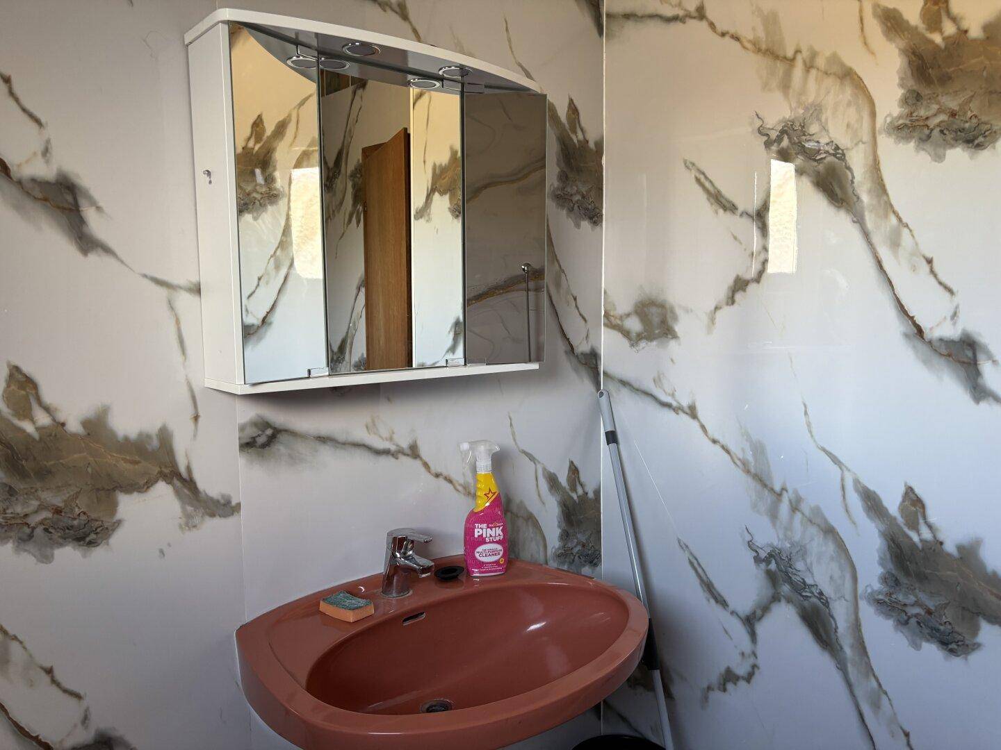 Badezimmer mit einem roten Waschbecken, Spiegelschrank und Marmor-Effekt-Fliesen an den Wänden.
