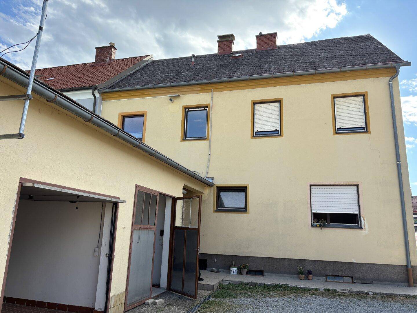 Gelbes Wohngebäude mit mehreren Fenstern und Rollläden, daneben eine angebaute Garage.