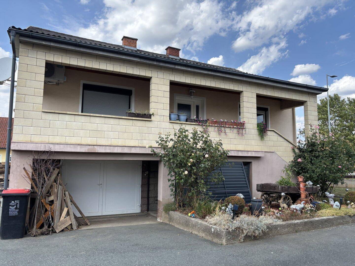 Vorderansicht des Hauses mit Balkon, Garage im Untergeschoss und Vorgarten.