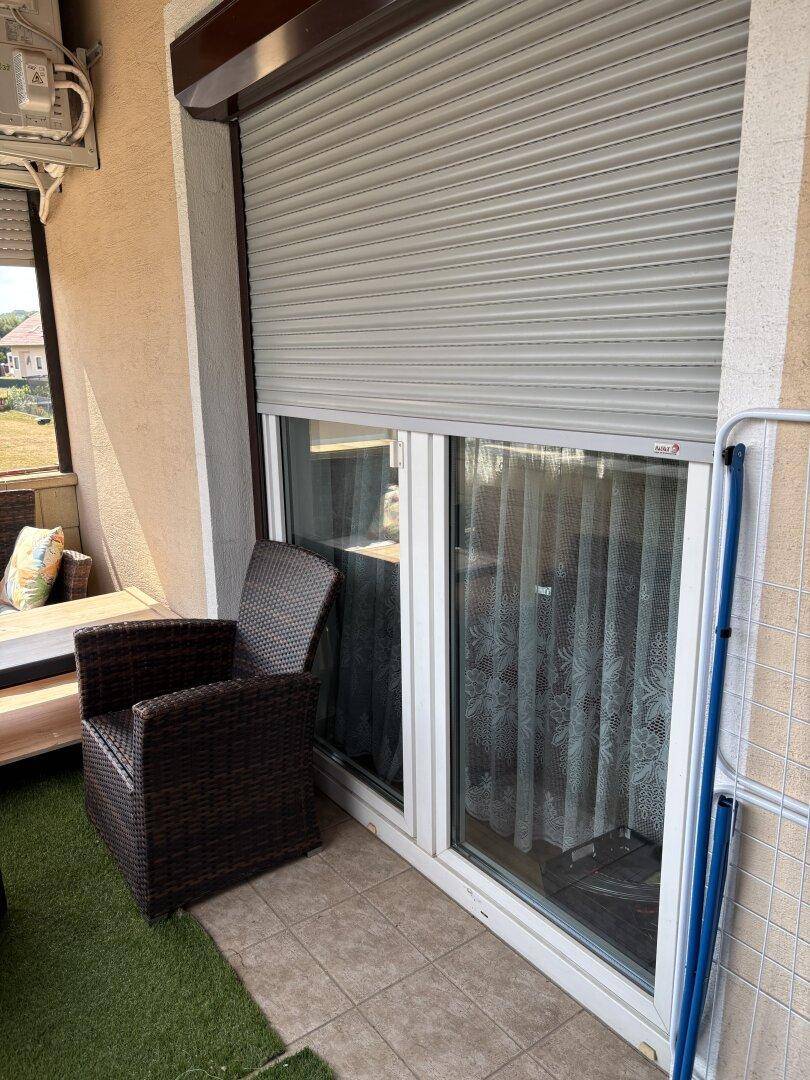 Detailansicht des Balkons mit Rollladen, Fliesenboden und Sitzgelegenheit.