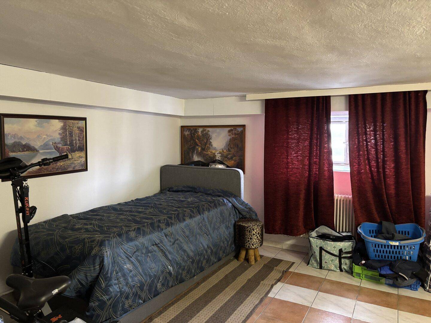 Kellerraum mit Bett, Bildern und Vorhängen, als zusätzlicher Wohnraum genutzt.