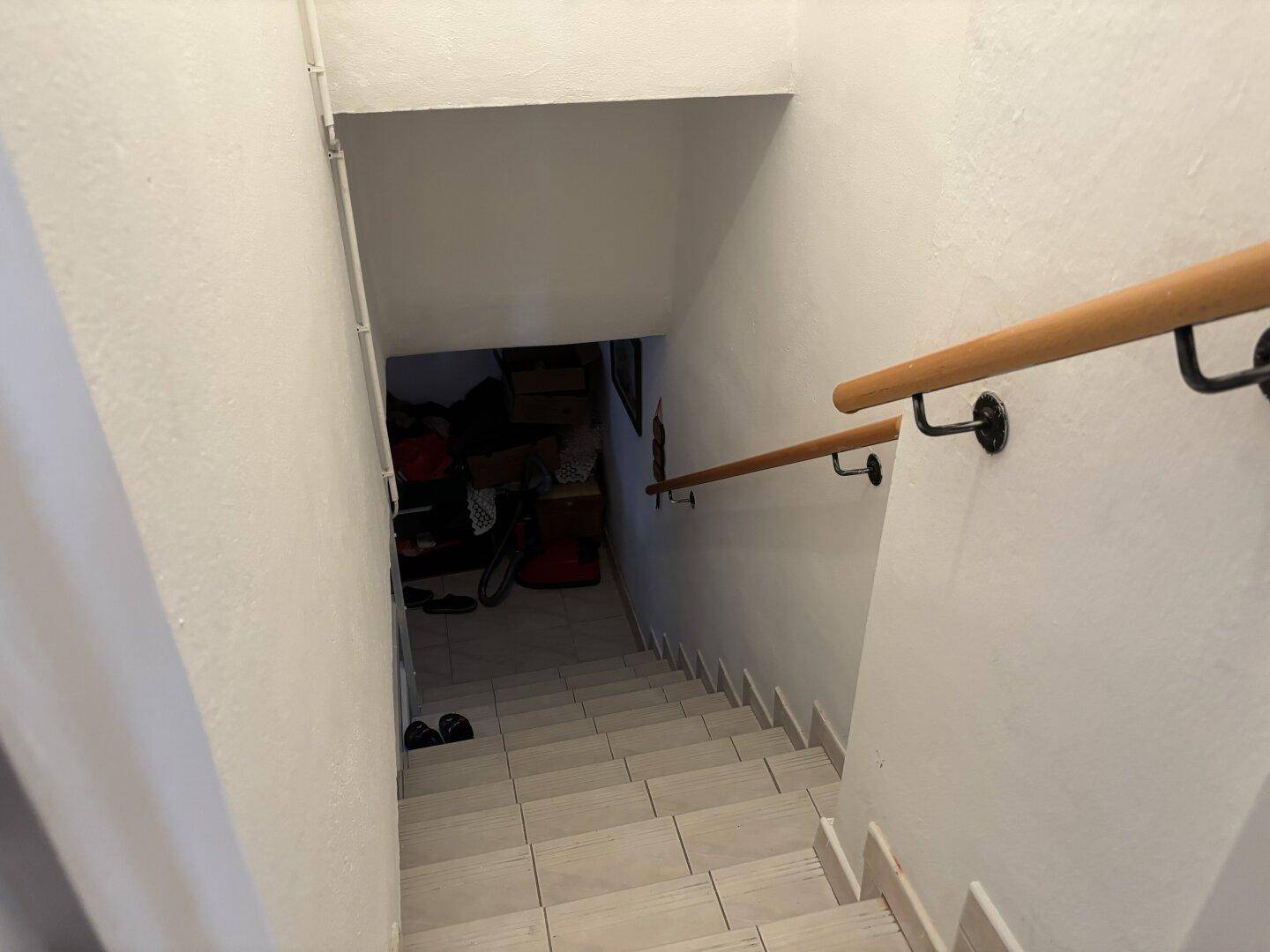 Treppenabgang in den Keller mit Fliesenstufen und Holzhandlauf.