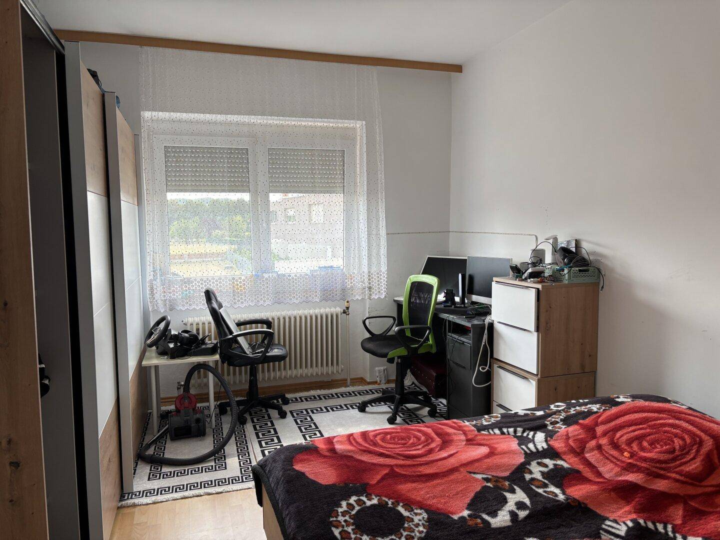 Schlafzimmer mit Bett, Schreibtisch und Blick auf die Umgebung durch das Fenster.