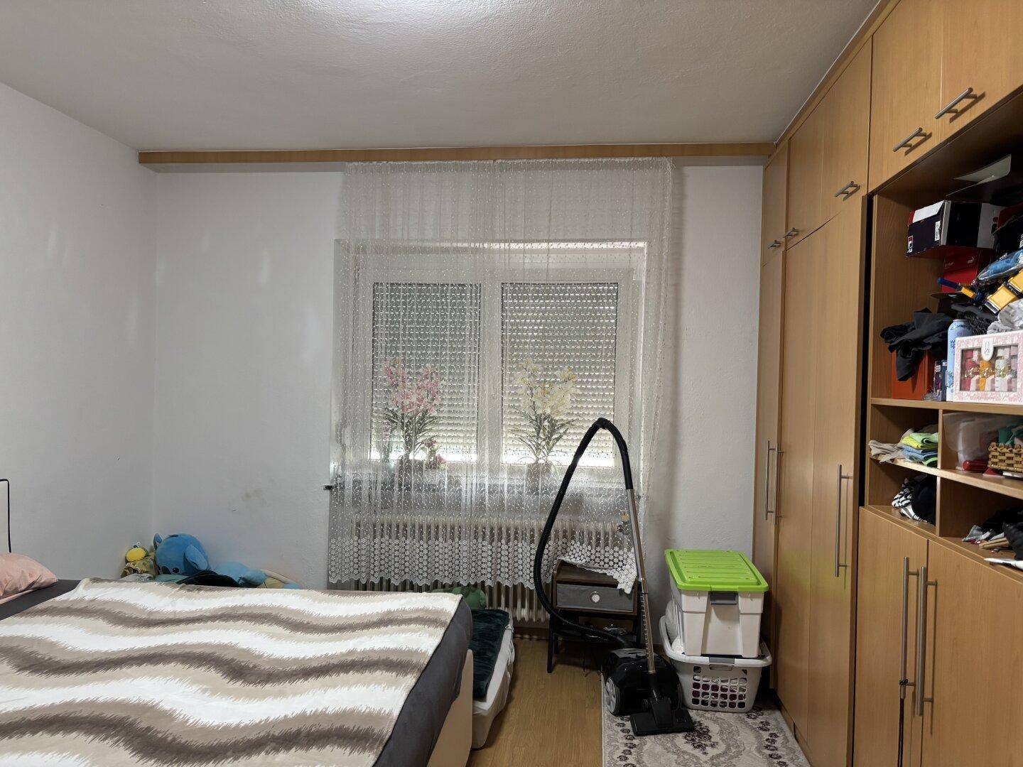 Schlafzimmer mit Bett, Kleiderschrank und Fenster mit Rollladen.