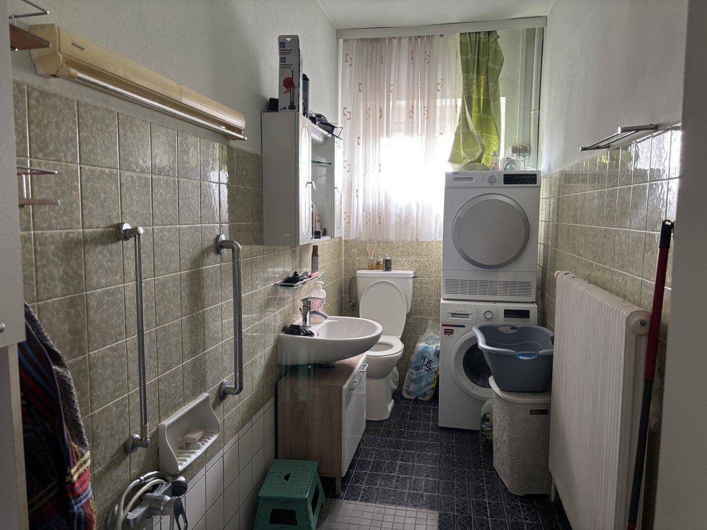 Funktionales Badezimmer mit Fliesen, Waschmaschine, Trockner und Duschbereich.