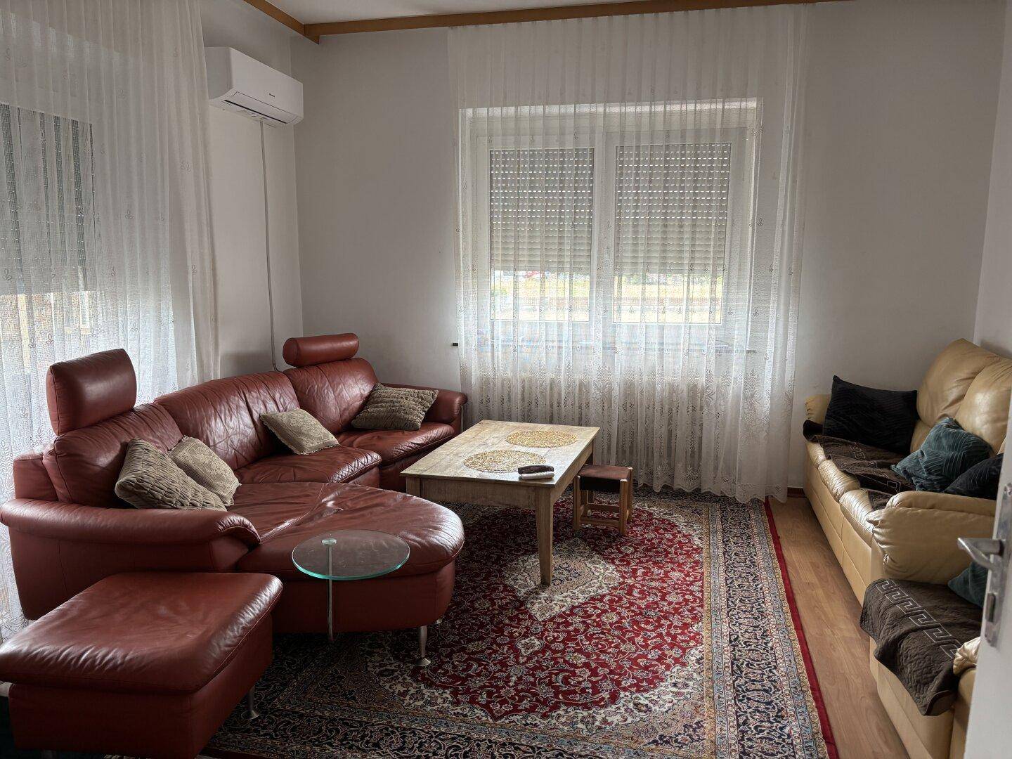 Gemütliches Wohnzimmer mit Ledersofas, Teppich und Blick nach draußen.