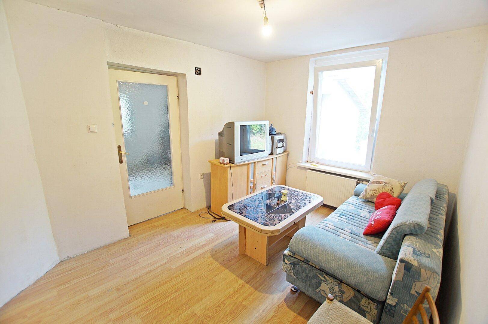 Helles Wohnzimmer mit Laminatboden, Sofa und Fenster mit Blick ins Grüne.