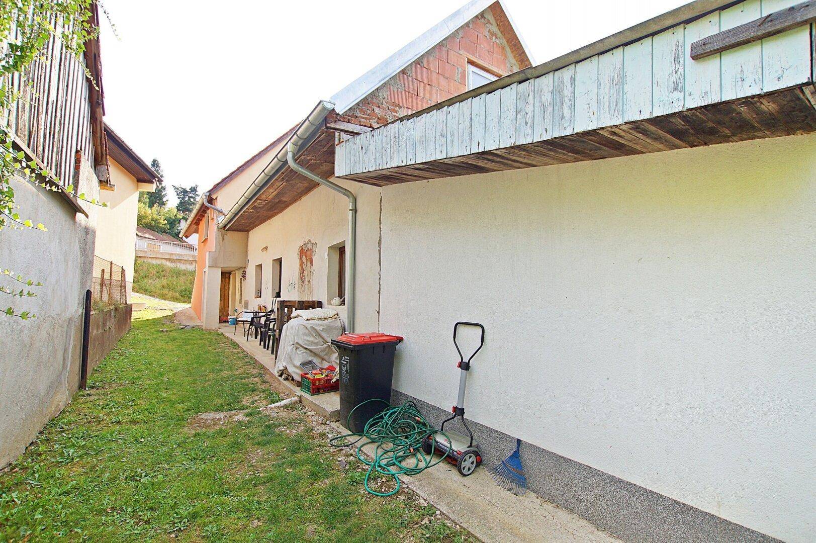 Seitenansicht des Hauses mit schmalem Gartenstreifen und Abstellbereich im Freien.