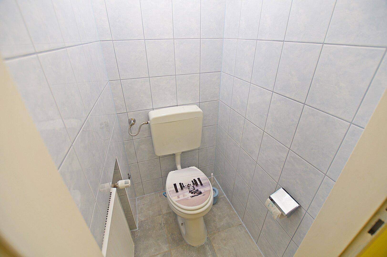 Separate Toilette mit weißen Fliesen an Wänden und Boden, sauber und funktional.