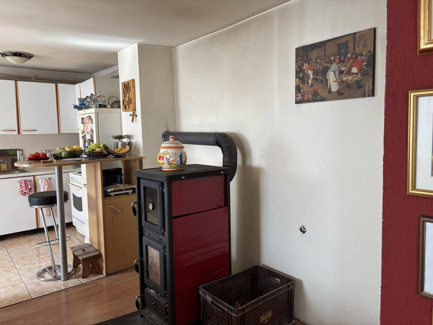 Kaminofen im Küchenbereich mit einfacher Ausstattung und weißer Wand, die zum Essbereich führt.