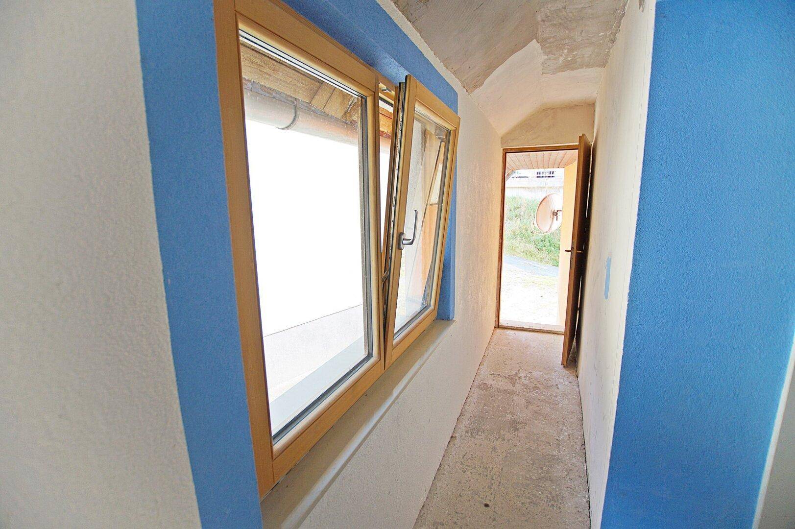 Schmaler Flur mit blauen Wänden, Holzfenstern und gewölbter Decke.