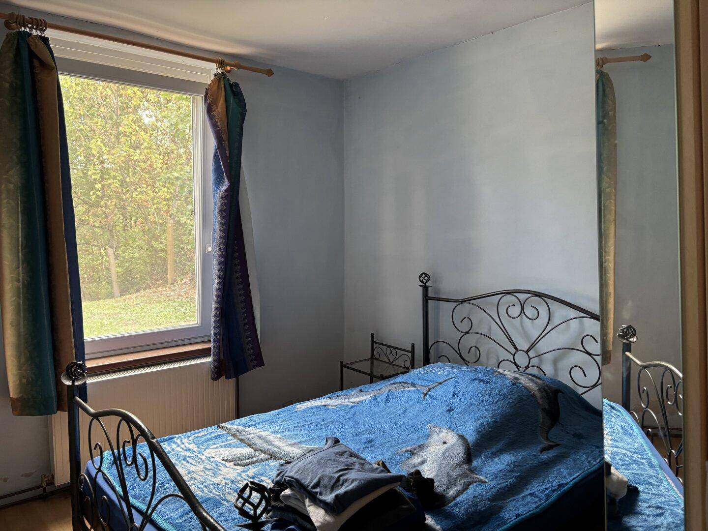 Schlafzimmer mit Metallbett, blauer Bettwäsche und Fenster mit Blick ins Grüne.