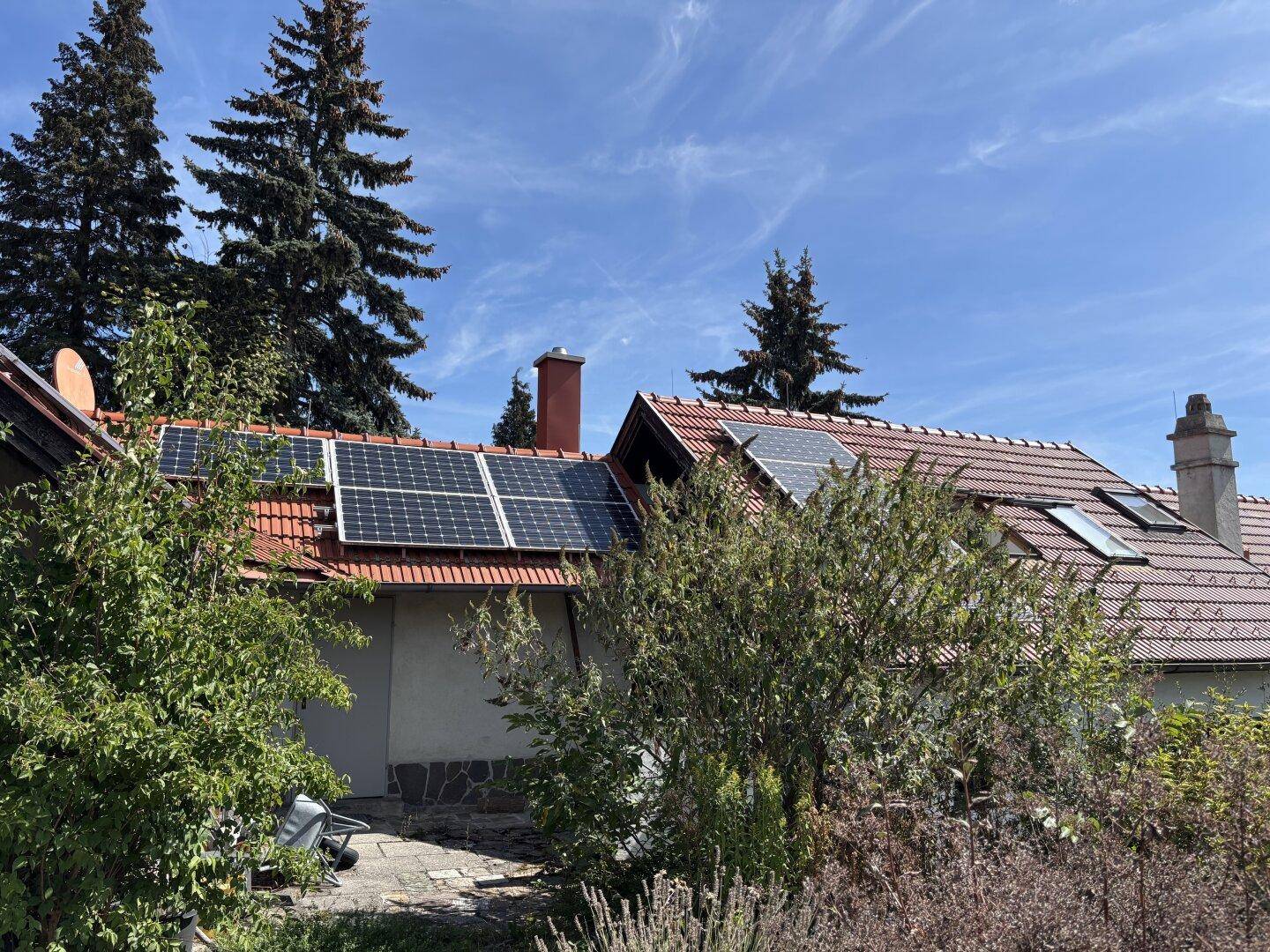 Dach eines Hauses mit Photovoltaikanlage und roten Ziegeln unter blauem Himmel.