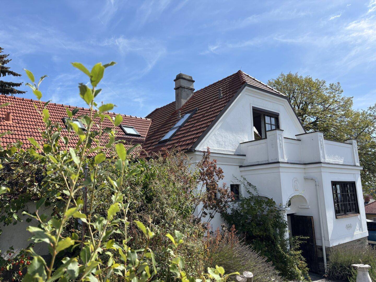 Charmantes Landhaus mit weißer Fassade, roten Ziegeldächern und Dachfenstern.