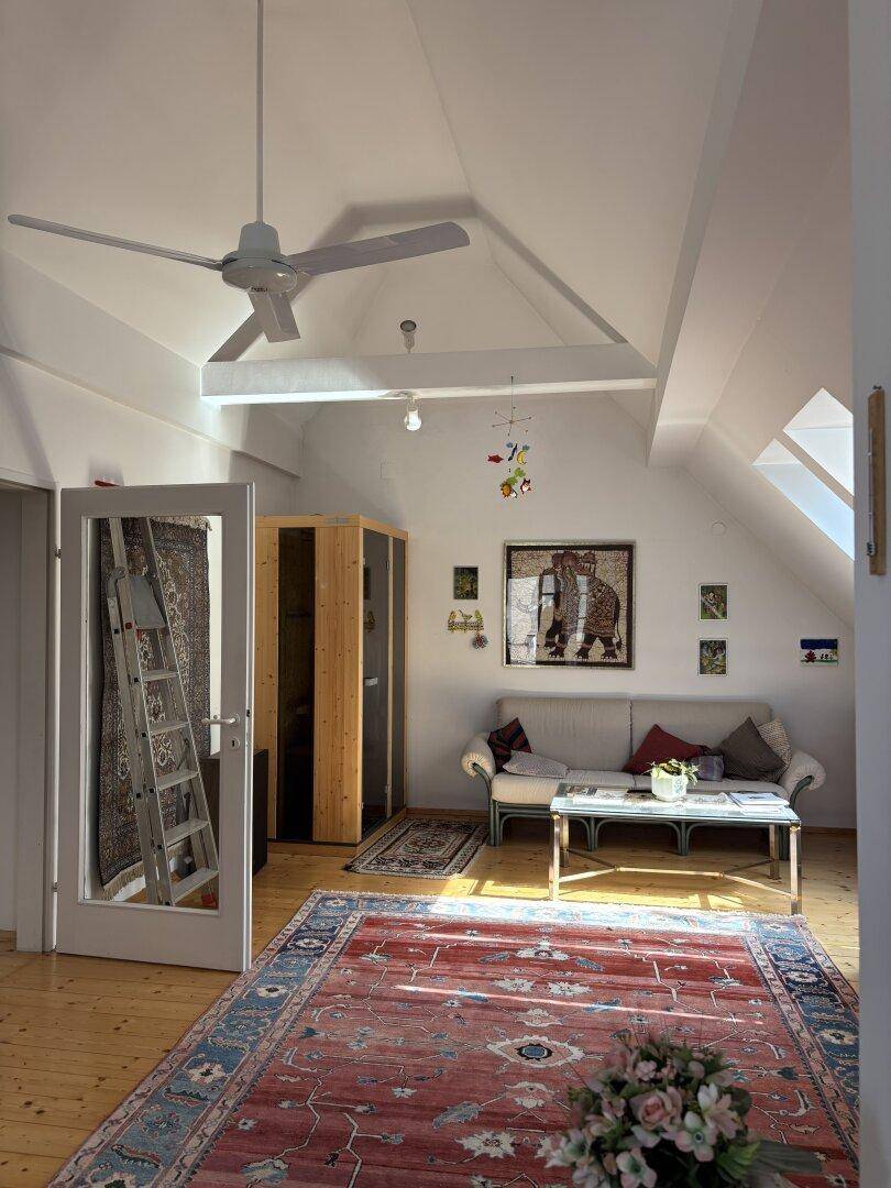 Helles Wohnzimmer im Dachgeschoss mit Dachschrägen, Holzboden und Deckenventilator.