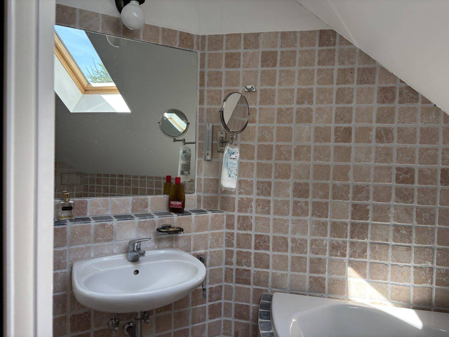 Helles Badezimmer im Dachgeschoss mit Dachfenster, kleinen Fliesen und Waschbecken.