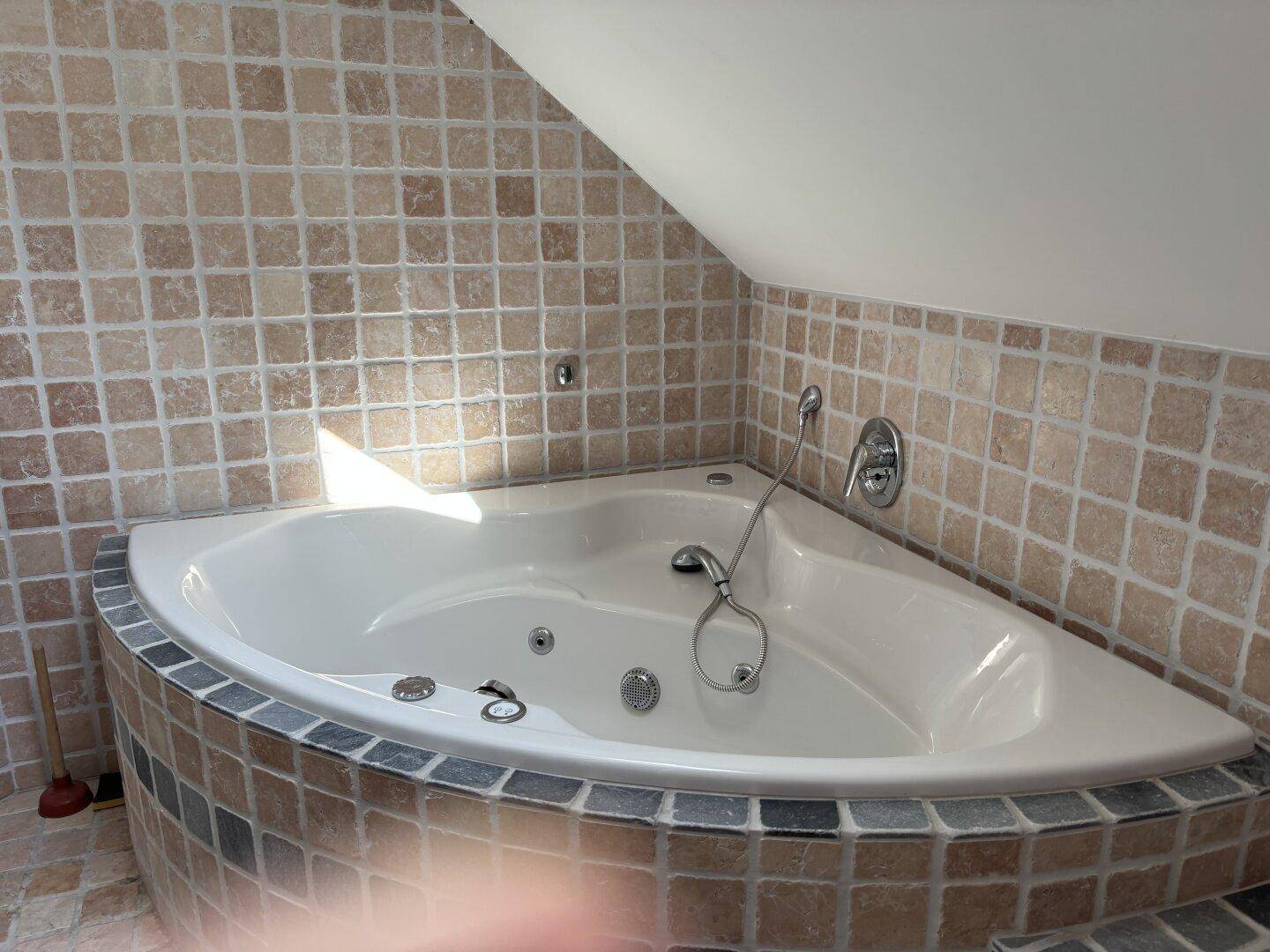 Gemütliches Badezimmer mit Eckbadewanne und beigefarbenen Fliesen unter einer Dachschräge.
