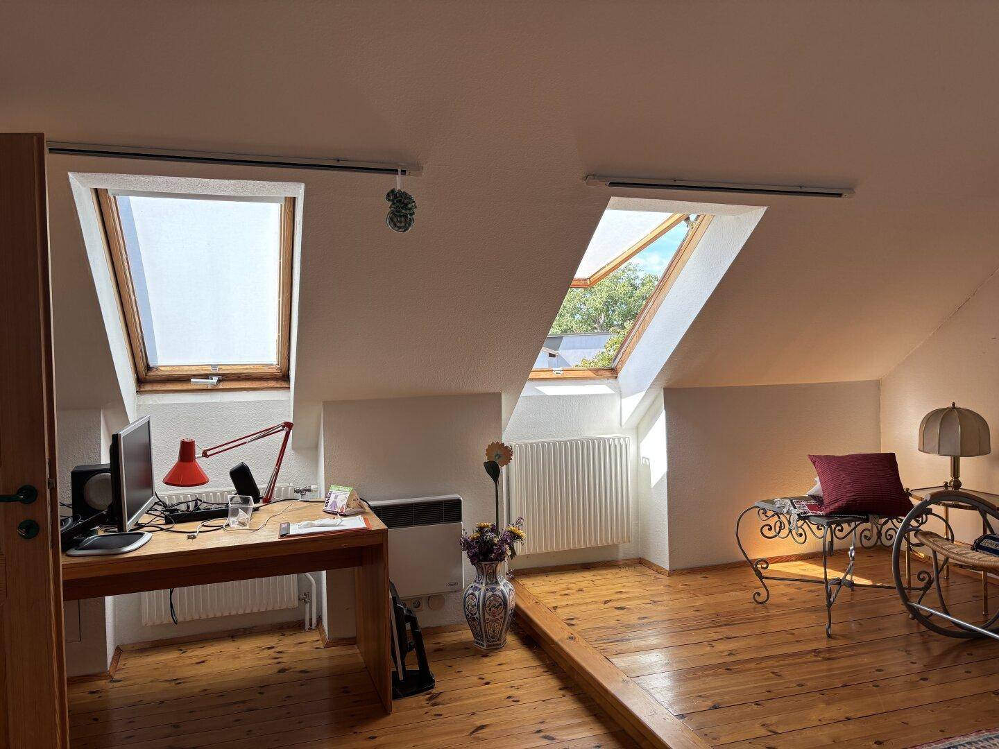 Dachgeschoss-Arbeitszimmer mit Holzboden, Schreibtisch und mehreren Dachfenstern für viel Tageslicht.