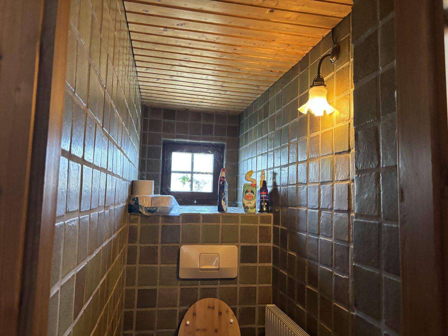 Kleines Gäste-WC mit grünen Fliesen, Holzdecke und einem kleinen Fenster für natürliche Belüftung.
